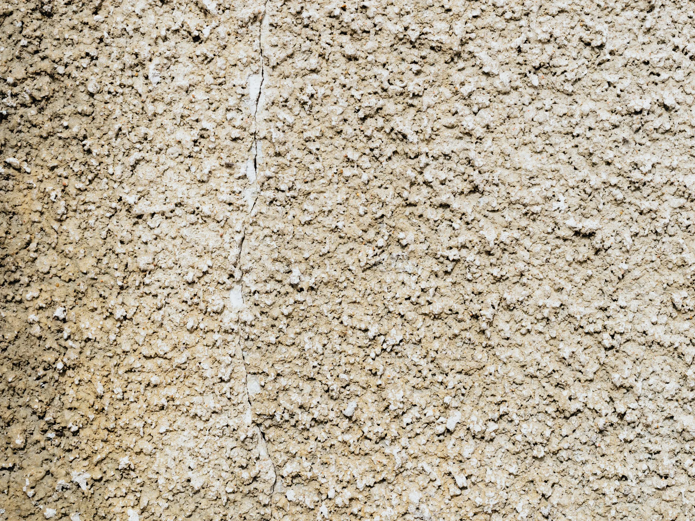 Stock photo: close-up of a rough, sand-colored textured wall with a fine crack running down it.