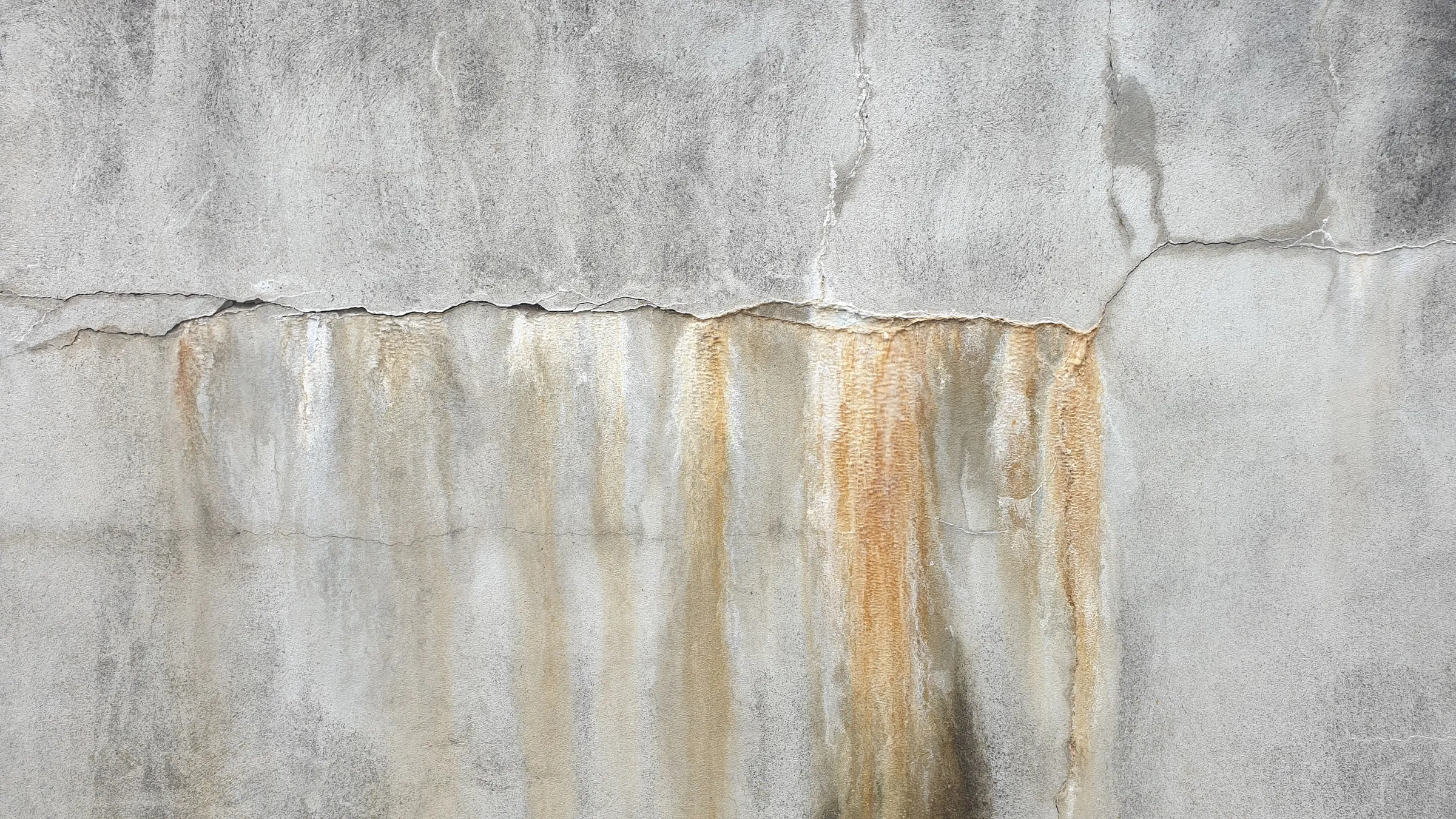 Stock photo: a gray rendered wall with a horizontal crack and rust-colored streaks running down the wall below it.